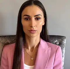 Woman in pink blazer, neutral expression.