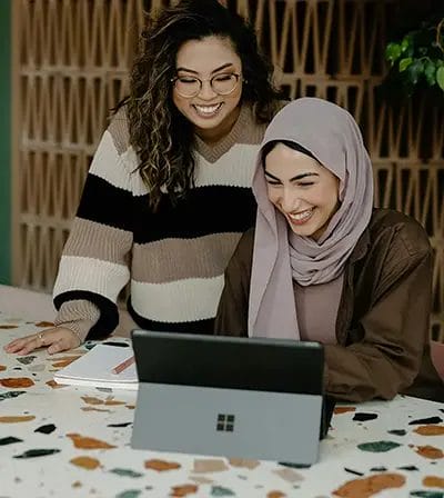 Two women smiling, working on a tablet.