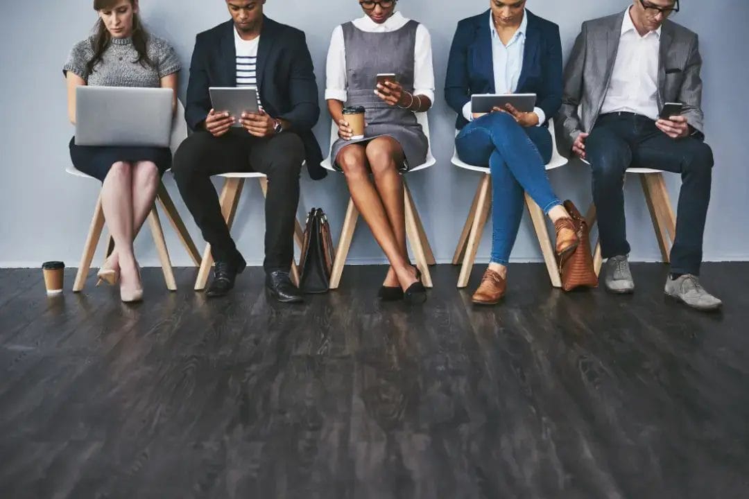Diverse group using devices, waiting together.